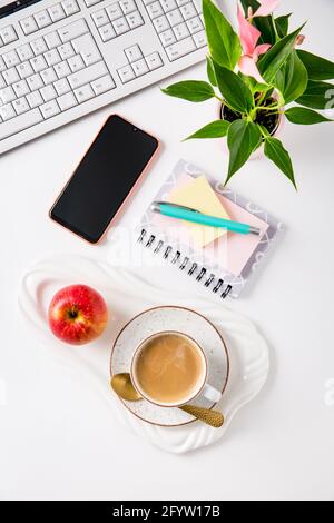Scrivania da lavoro e da ufficio con caffè, mela, computer portatile, cuffie e smartphone. Flatlay su sfondo bianco. Foto Stock