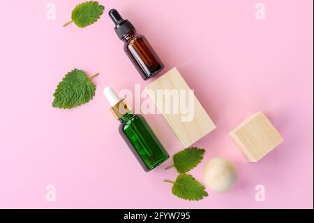 Vista dall'alto della menta verde fresca o delle foglie di menta verde e delle bottiglie di vetro contagocce di olio essenziale di menta su sfondo rosa. Erbe aromatiche naturali p Foto Stock