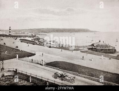 Una vista del tardo 19 ° secolo del Hoe a Plymouth, una città portuale nel Devon sulla costa meridionale dell'Inghilterra, dove Sir Francis Drake apparentemente insistito per completare il suo gioco di bocce prima di impegnare l'Armada spagnola nel 1588. Il grande molo del piacere, iniziato nel 1880, forniva una sala da ballo, rinfreschi, passeggiata e un punto di approdo per le gite in barca, ma fu bombardato nella seconda guerra mondiale A sinistra si trova il faro Eddystone di John Smeaton. Originariamente costruito nel 1759 sulle Eddystone Rocks, a 14 miglia a sud, fu smantellato nel 1877 e trasferito alla Hoe dove fu rieretto. Foto Stock