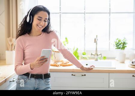 Passatempo preferito. Happy Brunette Lady in cuffie wireless ascolto di musica sullo smartphone Foto Stock