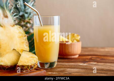 Succo di ananas in bicchiere con ingredienti. Bicchiere di cocktail al succo di ananas naturale fresco con tubo riutilizzabile in metallo su tavolo di legno marrone. RAW Foto Stock