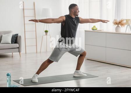 L'uomo afroamericano che fa lo Yoga in piedi nella posa del Guerriero indoor Foto Stock