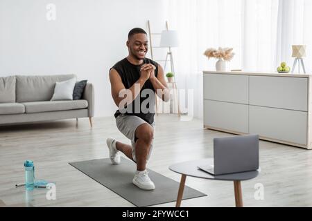Black Man facendo avanti Lunge esercizio vicino laptop a casa Foto Stock