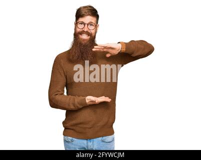 Giovane irlandese rosso uomo che indossa abiti casual e bicchieri gesturing con le mani mostrando grande e grande segno di misura, misura simbolo. Sorridente guardando th Foto Stock