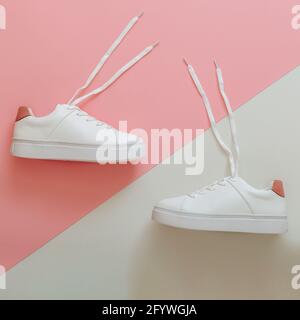 Sneaker bianche con lacci volanti. Paio di eleganti sneakers comode scarpe da donna hipper sportive. Scarpe donna in pelle bianca con lacci su rosa Foto Stock