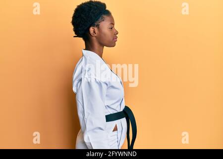 Giovane afroamericana che indossa kimono karate e cintura nera guardando a lato, rilassare profilo posa con viso naturale con sorriso fiducioso. Foto Stock