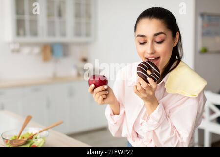 Donna sorridente che tiene la mela rossa e la ciambella mordente Foto Stock