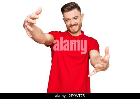 Giovane uomo rosso che indossa abiti casual guardando la macchina fotografica sorridente a braccia aperte per abbraccio. Espressione allegra che abbraccia la felicità. Foto Stock