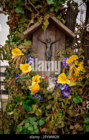 Una foto verticale di una piccola statua di Gesù Cristo su un albero decorato con fiori colorati Foto Stock