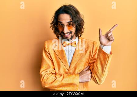 Giovane uomo ispanico che indossa hipster elegante look sorridente puntamento felice con la mano e il dito di lato Foto Stock