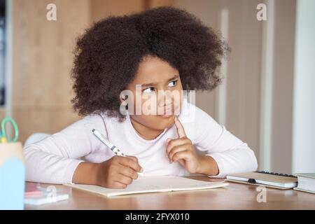 Pensiva piccola ragazza afroamericana pensando al compito di scuola dura siediti alla scrivania Foto Stock