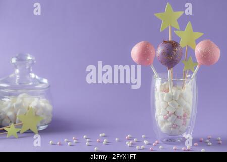 la torta smaltata si apre in un bicchiere e in un vasetto con marshmallows su sfondo viola con spruzzi. concetto di barretta caramella. immagine orizzontale. posto per il testo. Foto Stock