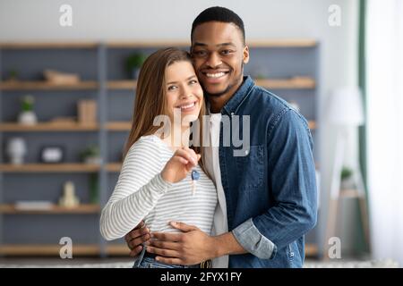 Concetto di alloggiamento. Portarit di giovani sposi interaciali felici che tiene le chiavi di casa Foto Stock