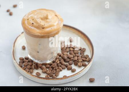 Caffè freddo Dalgona con panna montata in un bicchiere su uno sfondo di chicchi di caffè. Bevande estive a base di ghiaccio. Primo piano. Immagine orizzontale. Spazio per la copia Foto Stock