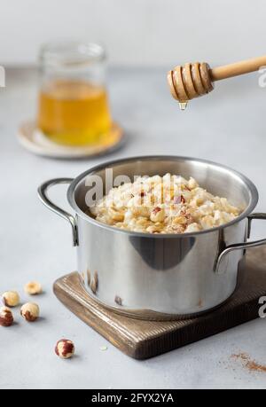 il miele gocciola da un cucchiaino di miele in legno in padella con porridge d'avena, condito con nocciole e cannella. concetto di cibo pulito. immagine verticale. Grigio Foto Stock