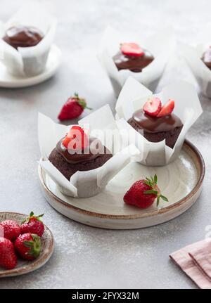 Deliziosi muffin al cioccolato decorati con salsa al cioccolato e fragole fresche. Panificio domestico. Immagine verticale. Sfondo grigio. Foto Stock