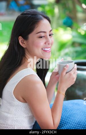 Lo stile di vita di una bella donna asiatica gode di caffè fresco la mattina a casa. Tempo felice della vita cittadina. Foto Stock