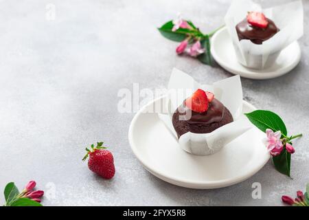 due muffin al cioccolato con sciroppo di cioccolato e decorato con fragole fresche. pasticceria per colazione o dessert. fondo in cemento grigio con posto Foto Stock