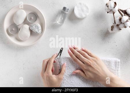 le mani della donna che tengono i tagliaunghie e tagliano la cuticola. cura della mano, manicure profonda. Sfondo in pietra bianca, vista dall'alto. Immagine orizzontale Foto Stock