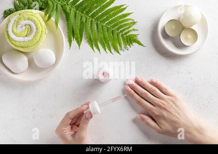 pipettare con collagene, siero ialuronico in una mano della donna. concetto idratante e di cura della pelle. Bellezza e sfondo spa con asciugamano, candele e felce Foto Stock