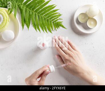 mani femminili che applicano siero alla pelle. routine di cura della pelle. sfondo bianco con candele e foglia verde. vista dall'alto. Foto Stock