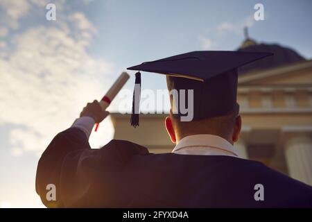 Studente di laurea in abiti tradizionali e cappello in piedi con rialzato diploma Foto Stock