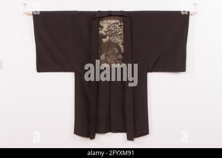Uomini di Haori con WAN Zixhi, WAN Xianzhi e il Padiglione delle Orchidee. Haori per un uomo con una decorazione al rivestimento di un paesaggio con padiglioni e un ponte su un ruscello in montagna, a imitazione di un dipinto a ventaglio pieghevole, con collegamenti due figure, l'uno (Xianzhi) inchiostro sfregando in una pietra d'inchiostro su una roccia , l'altro (Suo padre, Zixhi) scrivere con un pennello su un pezzo verticale di roccia. WAN Zixhi era un calligrafo cinese del IV secolo, famoso per la sua LAN TING XU, prefazione alla collezione di poesie scritte nel Padiglione delle Orchidee. Bruna di seta grezza (tsumugi) con decori testurizzati broccati Foto Stock