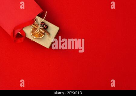 Borsa regalo con scatola decorata su sfondo rosso. Preparazione, acquisto di regali, vendita nel nuovo anno e Natale. Spazio di copia, vista dall'alto, disposizione piatta. Foto Stock