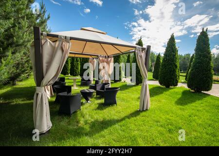 Gazebo in tela bianca con mobili da giardino in plastica in un prato verde estivo. Foto Stock