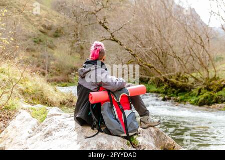 Seria giovane femmina in abiti casual che tengono retrò Instant film fotocamera in piedi sotto il cellofano trasparente in una stanza di colore rosso scuro durante lo sviluppo di foto Foto Stock