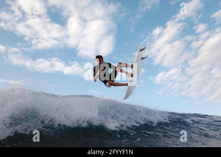 Giovane surfista maschile in surf praticando sport estremi in mare ondate sotto il cielo nuvoloso Foto Stock