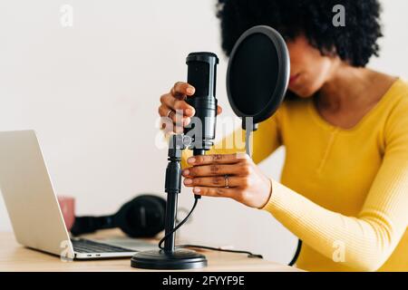 Crop Unriconoscable African American femmina musicista con capelli scuri ricci impostare il microfono prima di registrare la canzone in studio luce Foto Stock