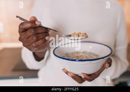 anonimo giovane afro-americana donna in abiti casual mangiando ciotola di muesli deliziosi Foto Stock