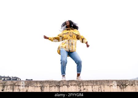 Corpo intero ad angolo basso della testa agitatrice femminile afroamericana mentre balla sul bordo di un percorso concreto Foto Stock