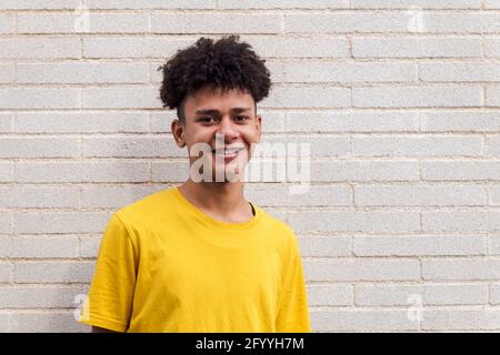 Allegro ragazzo afroamericano in abiti casual sorridendo felice in piedi contro muro di mattoni e guardando la fotocamera Foto Stock