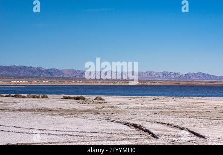 USA, CA, Salton Sea - 28 dicembre 2012: Lunga linea di scatole colorate sul treno merci passa lungo la linea costiera se sotto il cielo azzurro. Montagne su ho Foto Stock