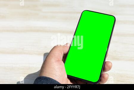 smartphone nero verticale con schermo verde cromato acceso un tavolo di legno chiaro in una giornata di sole Foto Stock