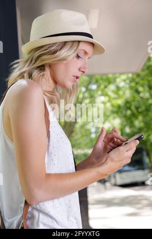 donna che legge il messaggio di testo mentre attende un bus Foto Stock