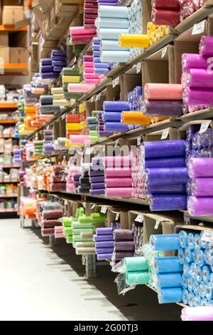 Negozio di tessuti con rotoli di tessuto su ripiani. Assortimento di abiti colorati in vendita in magazzino Foto Stock
