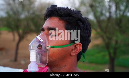 Giovane uomo inalare con maschera di ossigeno sul viso durante la pandemia in India. Una persona infetta con la malattia di Covid 19 al di fuori dell'ospedale. Coronavirus Foto Stock