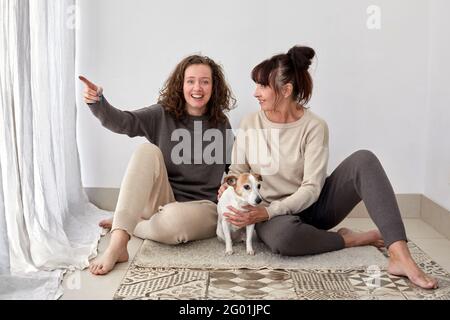 Allegra figlia adulta e madre di mezza età seduta sul pavimento con il cane carino a casa Foto Stock