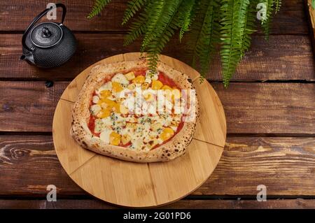 Pizza quattro formaggi su un supporto di legno Foto Stock