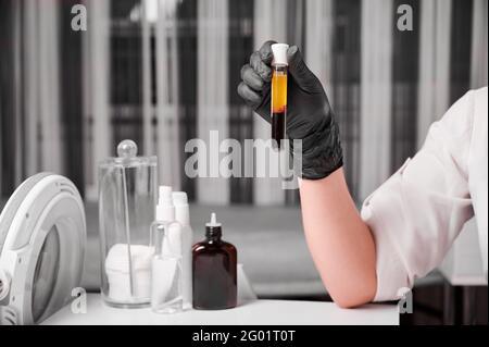 Primo piano delle mani di una donna scienziata in guanti neri che tengono una provetta per campioni di sangue da laboratorio. Ricercatore femminile che prepara materiale per il plasmolifting. Concetto di medicina clinica. Foto Stock