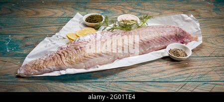 Filetto di pesce fresco crudo di pollock posto su tavolo di legno con set di erbe aromatiche e spezie per piatti sani fatti in casa ricetta Foto Stock