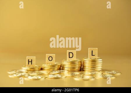 HODL scritto su blocchi di legno su pila di bitcoins su sfondo dorato. Acronimo che sta per 'Hold on for Ear life' nel concetto di criptovaluta. Foto Stock