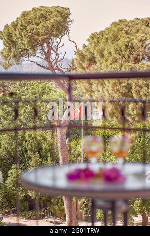 Cocktail estivi e fiori rosa di bougainvillea di fronte alla bandiera turca e le montagne. Concetto di viaggio Turchia. Mattina romantica al balcone. Foto verticale. Messa a fuoco selettiva Foto Stock