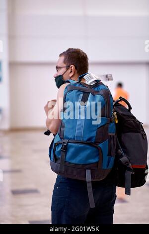 Passeggero mascherato con bagaglio nella lobby dell'aeroporto. Turismo durante una pandemia di coronavirus. Sfondo sfocato. Foto di alta qualità Foto Stock