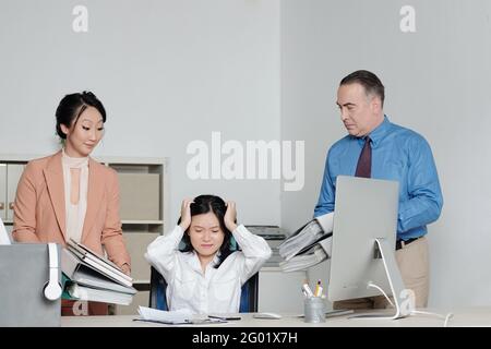 La giovane donna d'affari ha sottolineato e sopraffatta con l'ammount di lavoro, i suoi colleghi stanno dando le sue cartelle di documenti Foto Stock