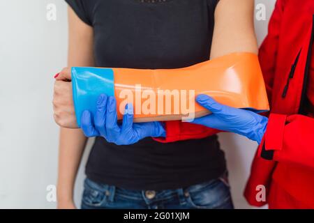 Primo piano del braccio rotto femmina nella colata di intonaco. Caucasica ferita Donna in T-Shirt nera seduta e tenuta polso in gesso bendaggio con dolore fisico Foto Stock