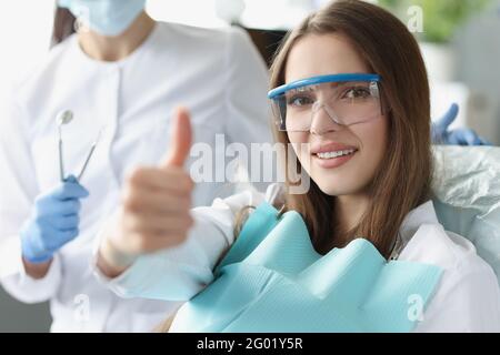 Ritratto di donna sorridente che tiene i pollici in su al dentista appuntamento Foto Stock